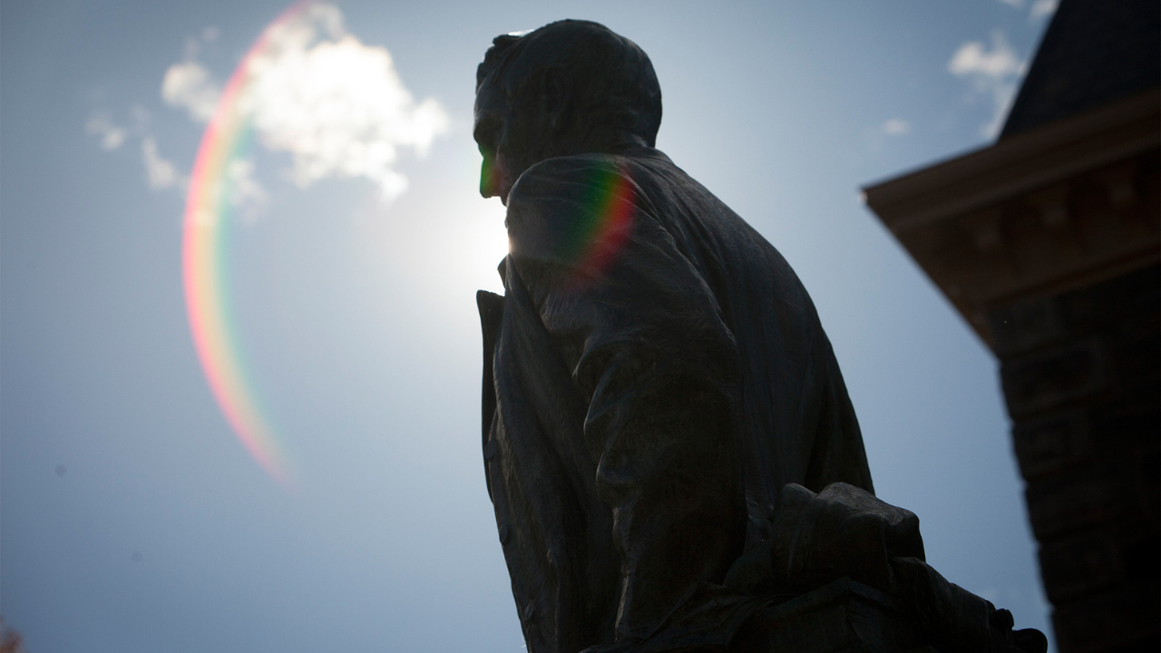 The statue of Ezra Cornell is taken from below, the sun shines behind it. 