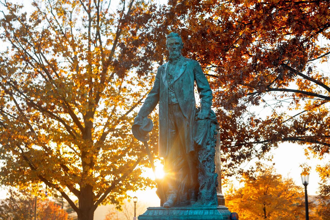 The Ezra Cornell Statue in the Arts Quad during an autumn sunset.