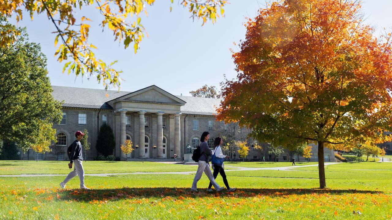 Students walk to class through the Arts Quad in peak autumn. Goldwin Smith Hall in the background.