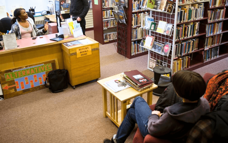 A student sits in a big comfy chair by the return area of the Alternatives Library.