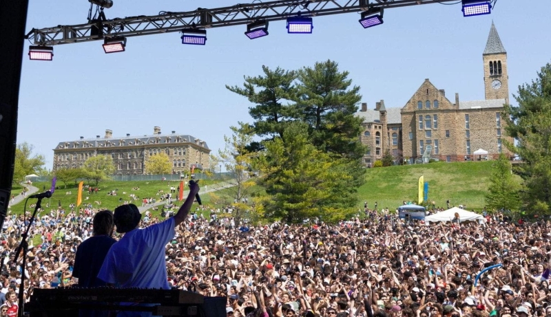 A performer on stage waves out at a huge crowd of Cornellians on the slope.