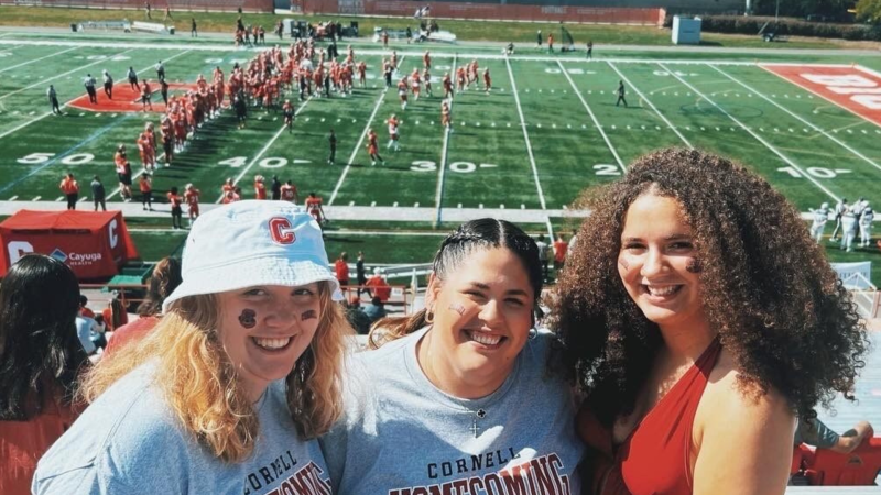 Arisbel and two friends smile from the stands during a football game at Schoellkopf Field.