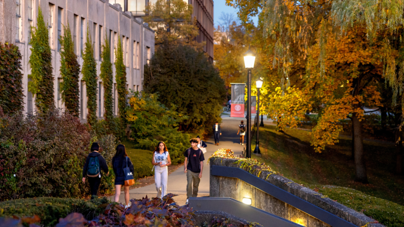 Students walk the pathway near Day Hall at dusk.