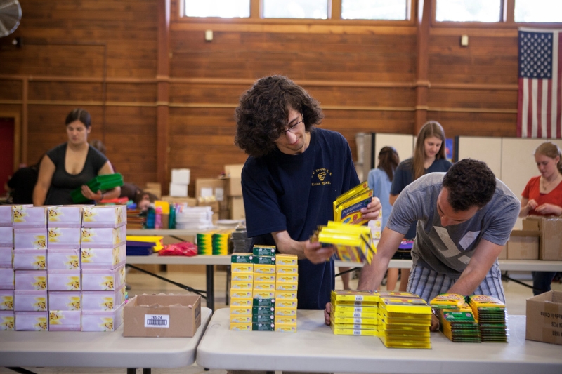 Pre-Orientation Service Trips (POST) student volunteers sorting books and backpacks at a local school.