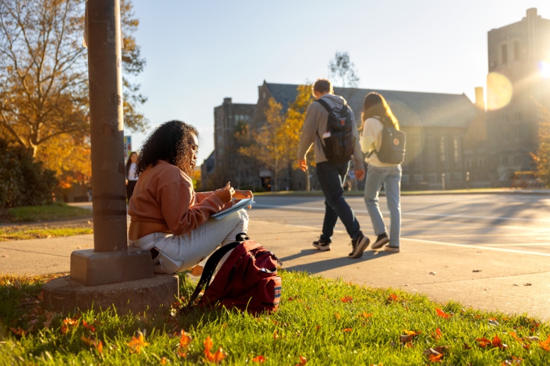 A student studies along College Avenue while waiting for a bus.