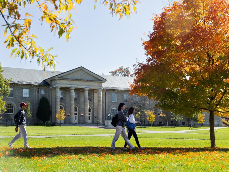 Students walk to class through the Arts Quad in peak autumn. Goldwin Smith Hall in the background.