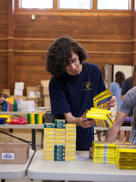 Pre-Orientation Service Trips (POST) student volunteers sorting books and backpacks at a local school.