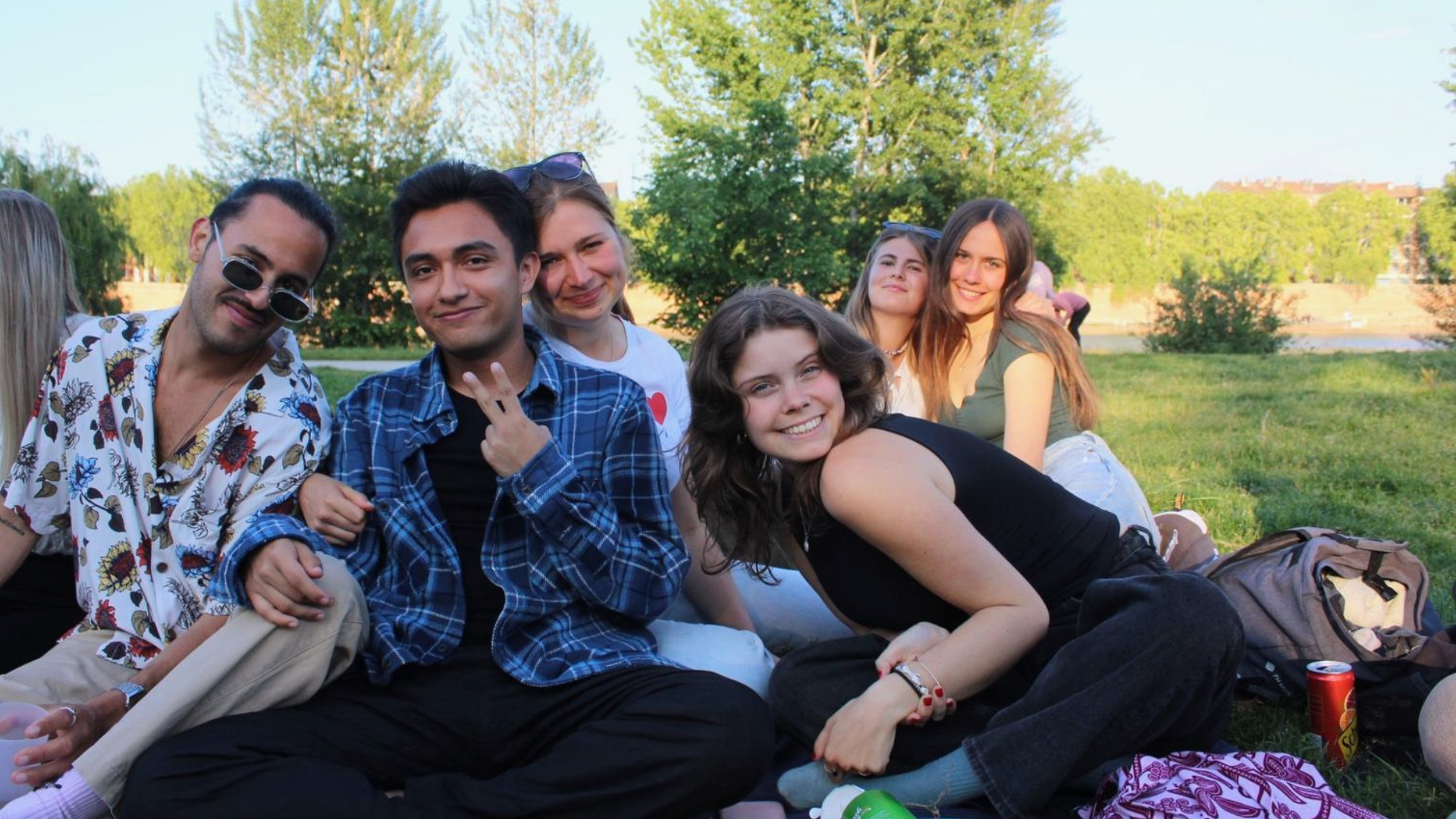 A group of students pose on a blanket while enjoying a picnic.